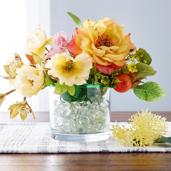 yellow faux flowers in glass vase with bead filler on table
